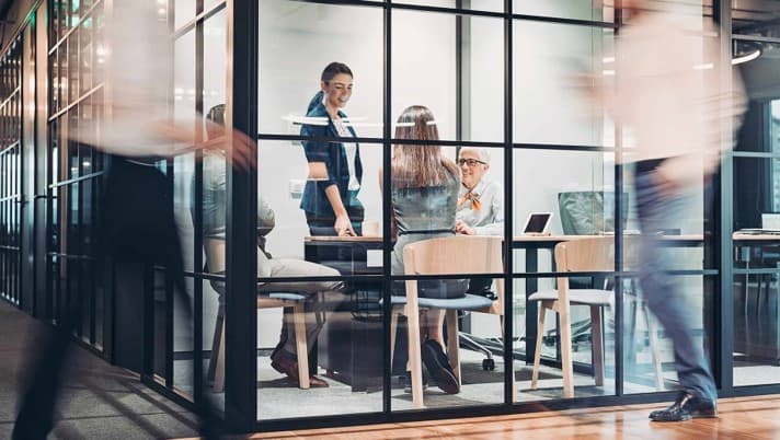 Team meeting in a glass-walled conference room with colleagues collaborating at a table